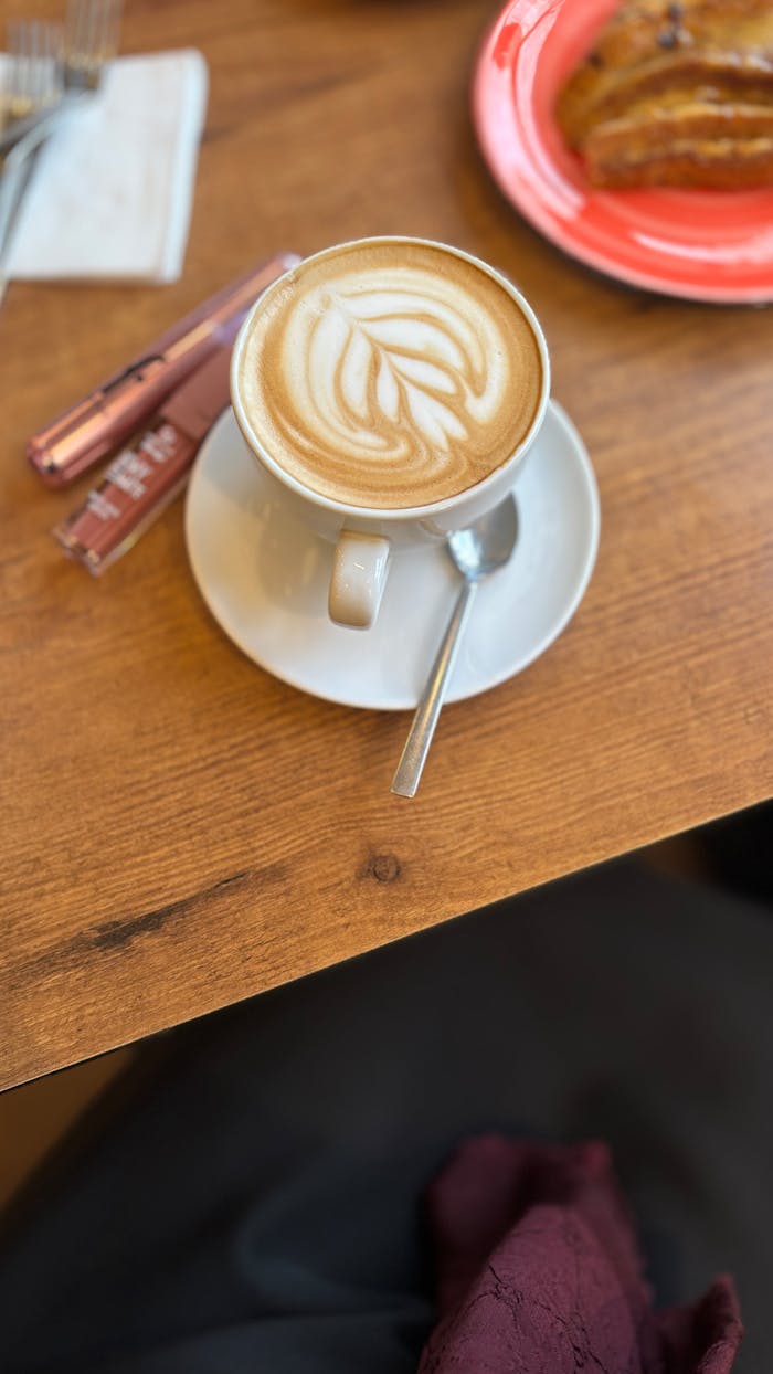 Top view of a latte with latte art and croissant on a wooden table.