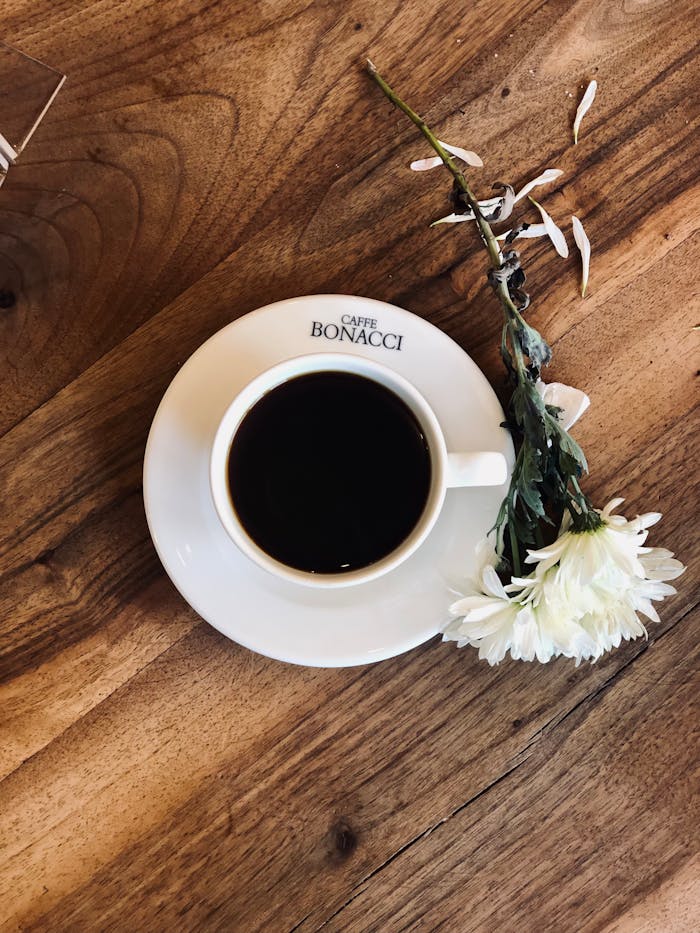 Top view of coffee cup with white flower on rustic wooden table, creating a warm and cozy vibe.